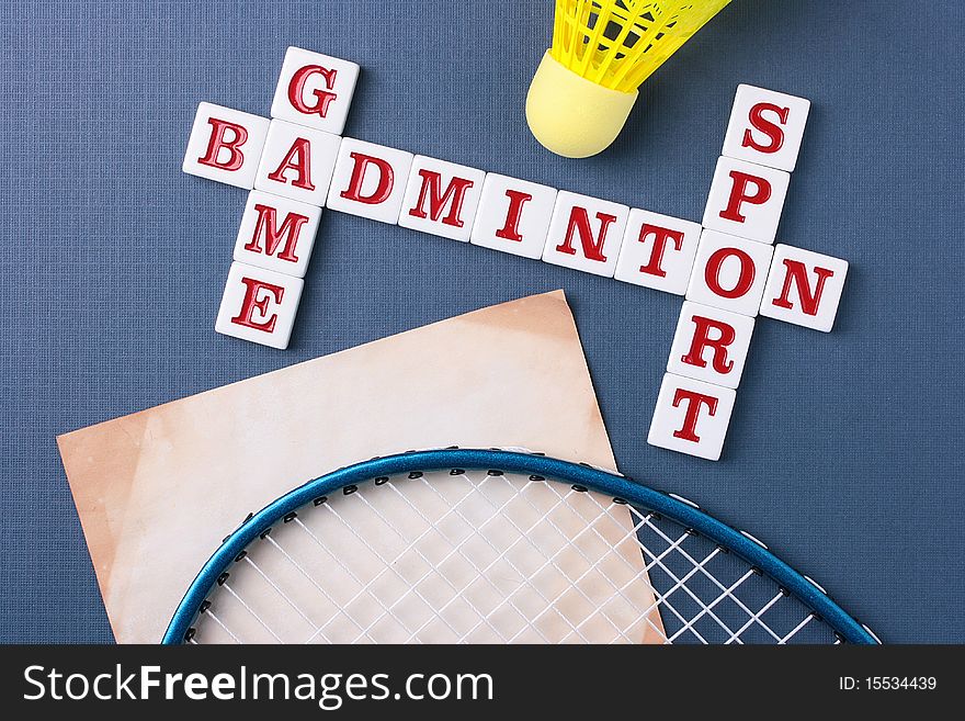 A yellow synthetic shuttlecock and a blue badminton racquet next to a badminton crossword.