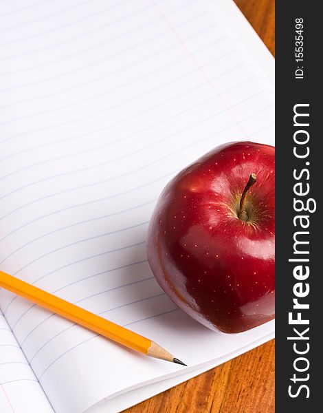 A red apple and pencil sitting on an opened notebook.  Concept of education. A red apple and pencil sitting on an opened notebook.  Concept of education.