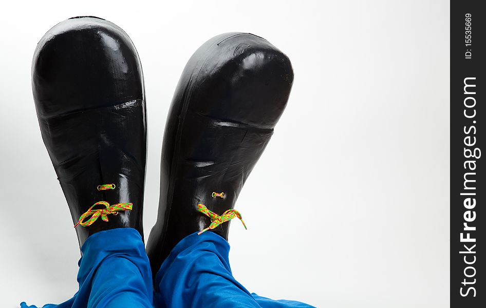 Black clown shoes and baggy blue pants against white background