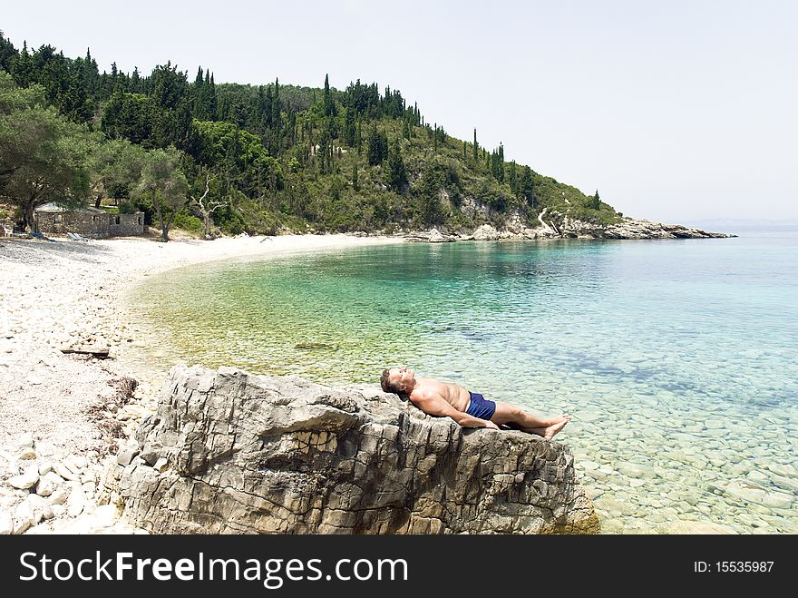 Color landscape photo of a caucasian man laying on rocks and sunbathing along a stunning beach in Paxos Greece. Color landscape photo of a caucasian man laying on rocks and sunbathing along a stunning beach in Paxos Greece.