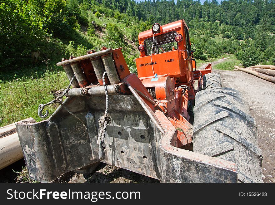 The jointed lumber tractor used for forest lumberings of any kinds. Wooden logs on the background. Wide shot. The jointed lumber tractor used for forest lumberings of any kinds. Wooden logs on the background. Wide shot.