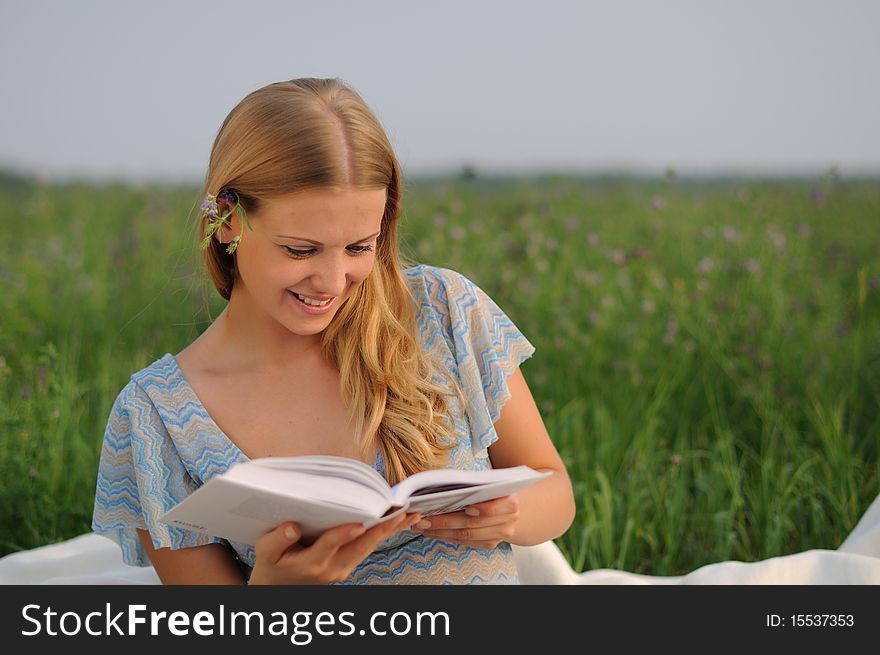 Young girl sitting on green grass and reading a book