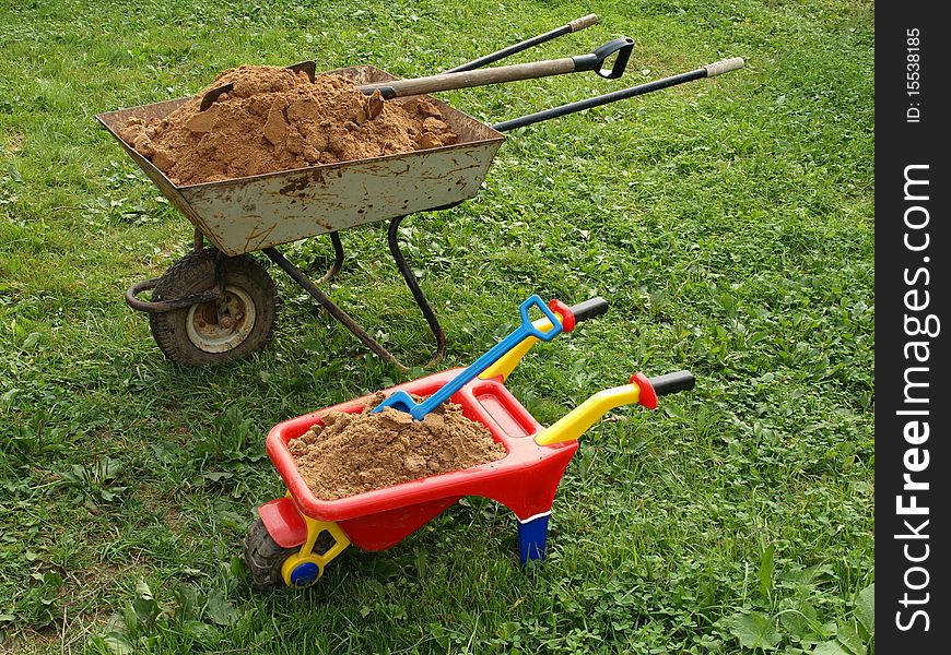 Two wheelbarrows with sand on green to a grass.