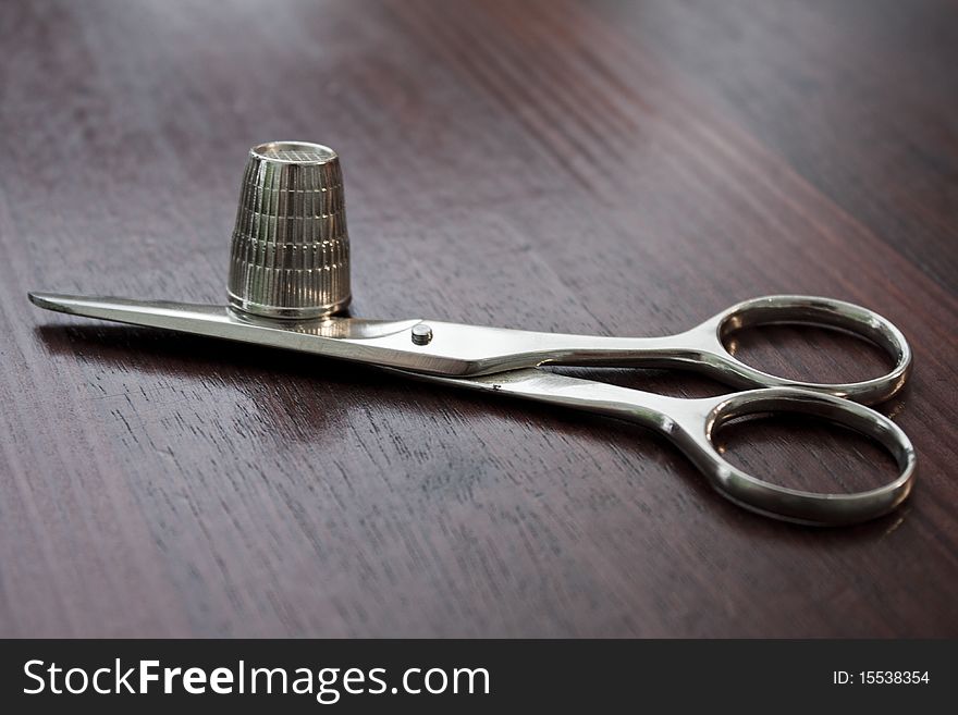 Metallic scissors and thimble on a table.