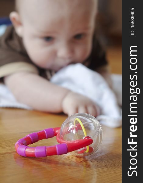 Baby boy in distance reaching for a toy rattle in the foreground. Baby boy in distance reaching for a toy rattle in the foreground