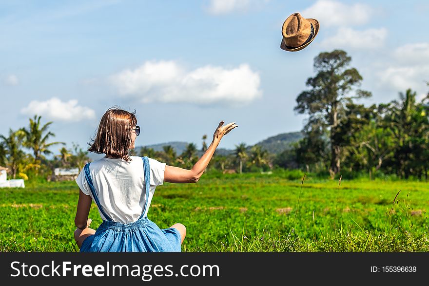 Tropical portrait of young happy woman with straw hat on a road with coconut palms and tropical trees. Bali island.