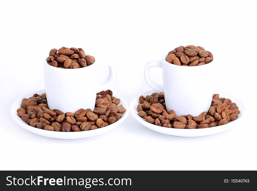 Two coffee cups and plates filled with roasted coffee beans. Two coffee cups and plates filled with roasted coffee beans