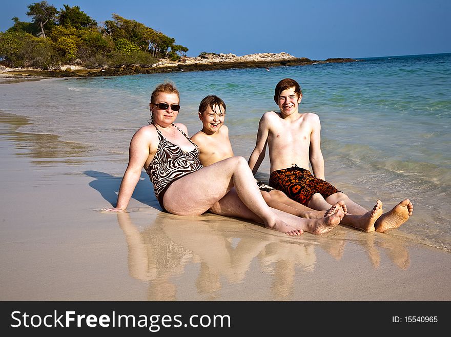 Family is sitting at the beautiful sandy beach and enjoying the sun and the water. Family is sitting at the beautiful sandy beach and enjoying the sun and the water