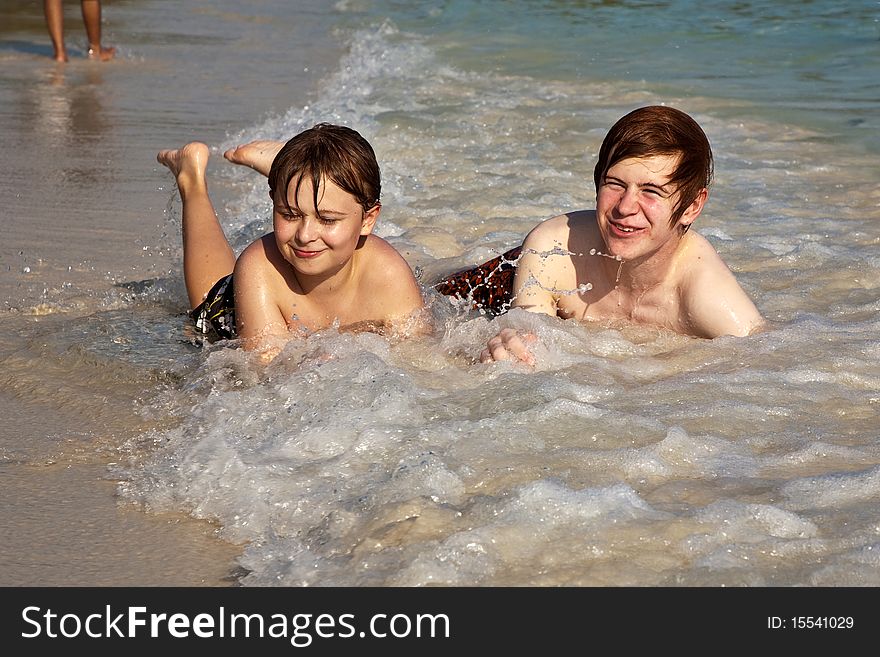 Brothers are lying at the beach  and enjoying the sun and the water