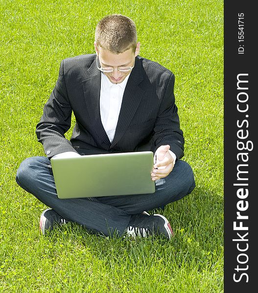 Young businessman sitting on grass with laptop