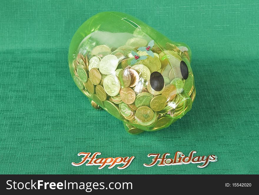 Piggy bank full of coins on a green textile with Happy Holidays. Piggy bank full of coins on a green textile with Happy Holidays