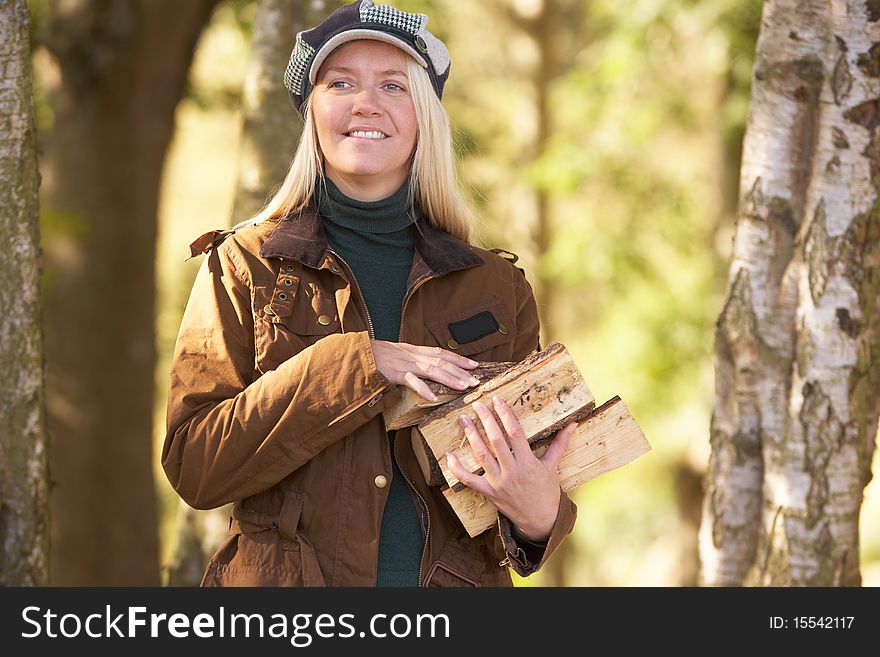 Woman Outdoors In Autumn Woodland Gathering Logs At Camera