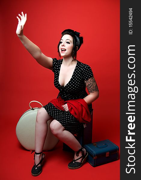 Beautiful young pinup girl sitting on luggage holding up hand. Beautiful young pinup girl sitting on luggage holding up hand