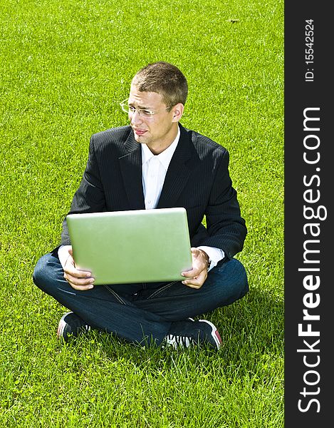 Businessman on grass with laptop, mixed feelings