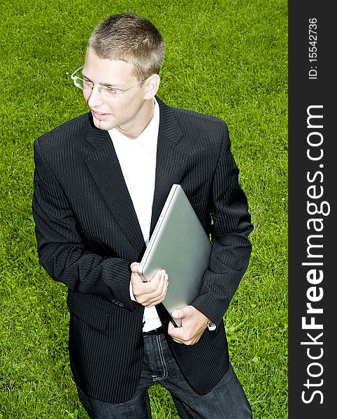Young businessman standing on the grass with his laptop, talking. Young businessman standing on the grass with his laptop, talking