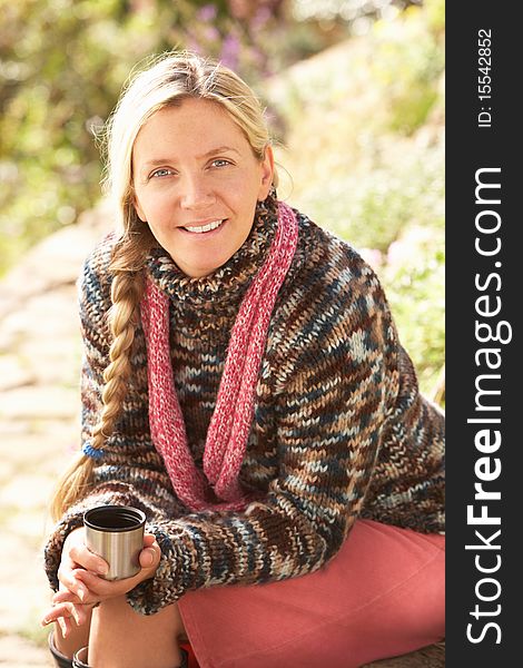 Young Woman Relaxing With Thermos Flask In Autumn Landscape