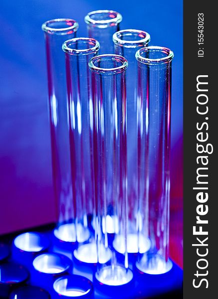 A set of bottom lighted empty glass test tubes in a rack with purplish blue background. A set of bottom lighted empty glass test tubes in a rack with purplish blue background