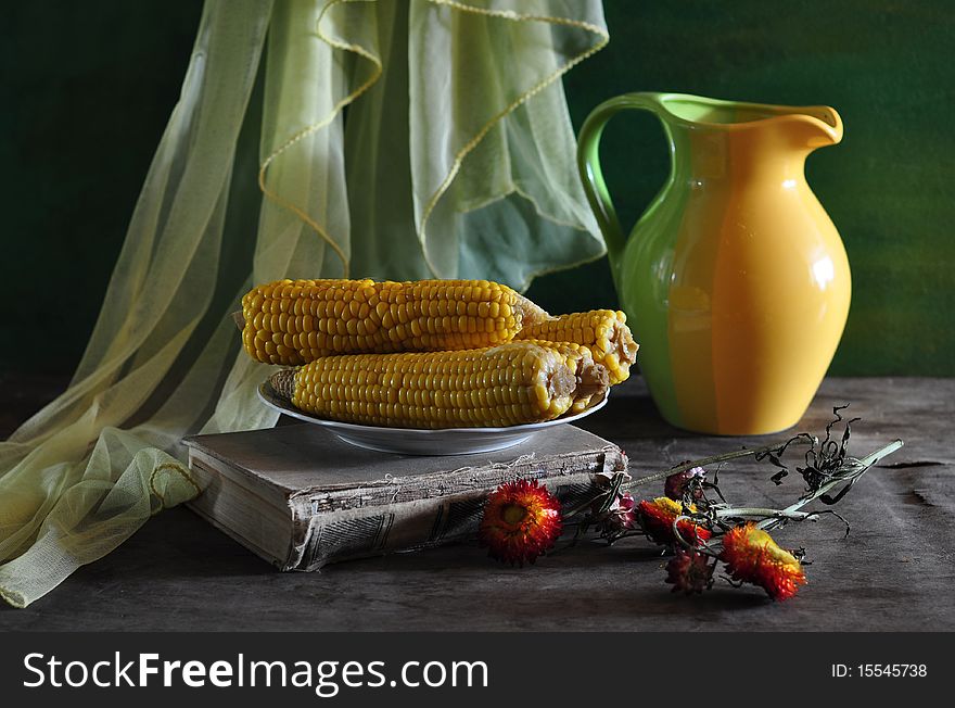 Corn-cobs, old book and jug, lie on an old table