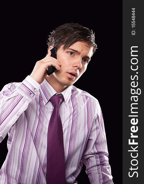 Portrait of a handsome young business man speaking on the mobile isolated on black background