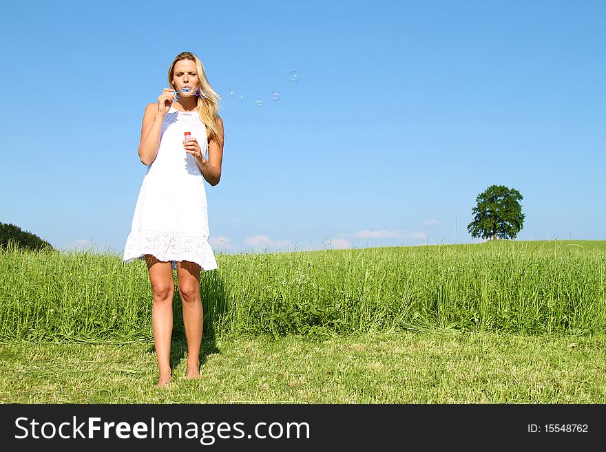 Beautiful blond girl standing outside in a white summer-dress and playing with soap bubbles. Beautiful blond girl standing outside in a white summer-dress and playing with soap bubbles