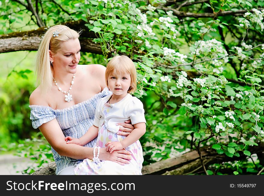Woman and her baby daughter sit on a tree trunk in a beautiful blooming garden. Woman and her baby daughter sit on a tree trunk in a beautiful blooming garden