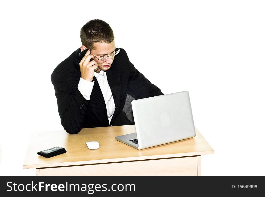 Young businessman working on desk with laptop, mouse and wallet, talking on mobile phone. Young businessman working on desk with laptop, mouse and wallet, talking on mobile phone