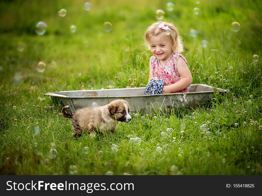 Little girl sits in a trough and washes a dress on a green meadow. next to a little puppy in the grass among the flowers. Simple r