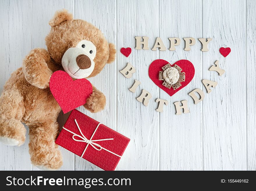 Toy bear with a heart and boxes with gifts on a light wooden background. The design of the birthday greeting card. Frame for the