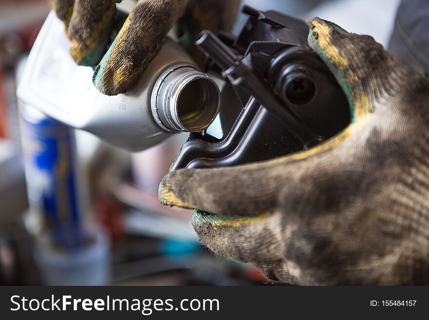 A mechanic in dirty gloves and overalls pours engine oil from a canister into the engine. The process of working in a service station.