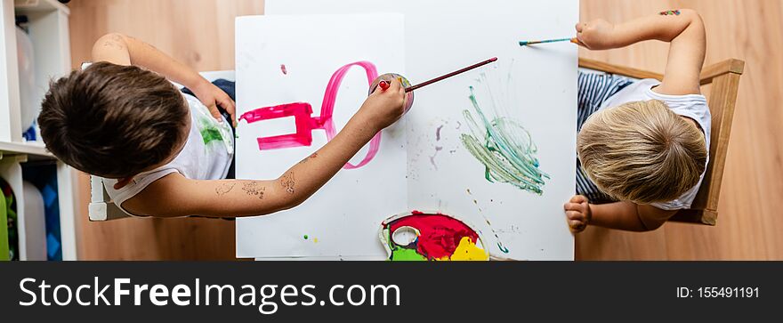 Wide view image of two toddler kids painting with colors using brushes. Top view