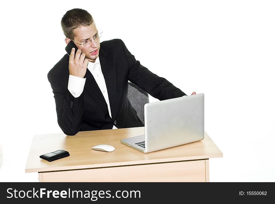 Young businessman irritated while working in office, looking at laptop and talking on mobile phone. Young businessman irritated while working in office, looking at laptop and talking on mobile phone