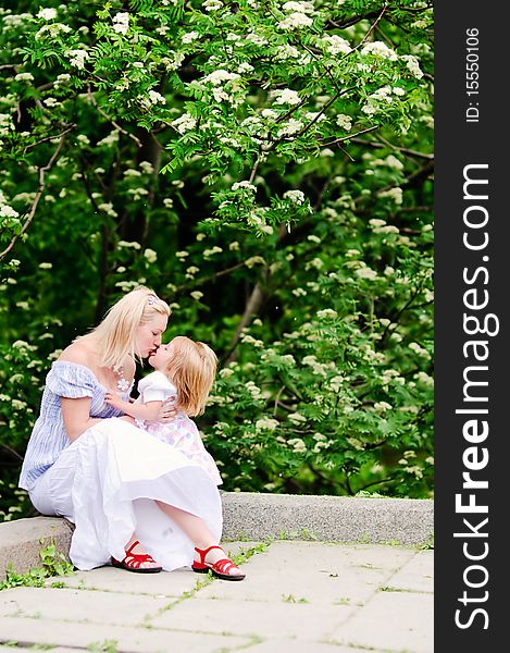 Beautiful blond woman and her baby daughter kissing in blooming garden. Beautiful blond woman and her baby daughter kissing in blooming garden