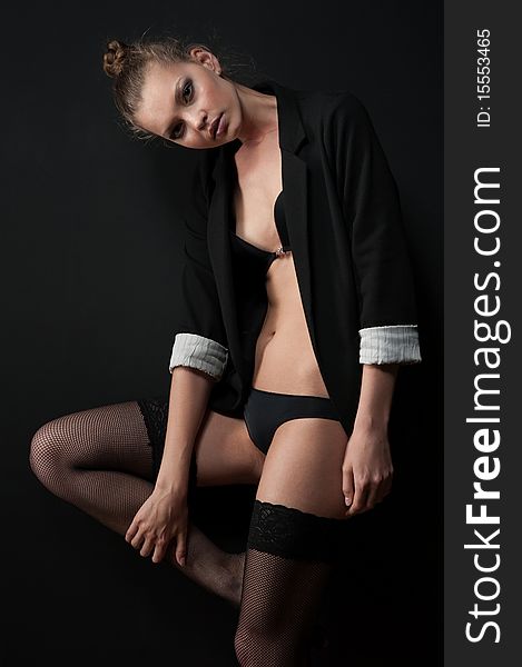 Amazing girl posing against the black wall in stockings and a jacket. Amazing girl posing against the black wall in stockings and a jacket