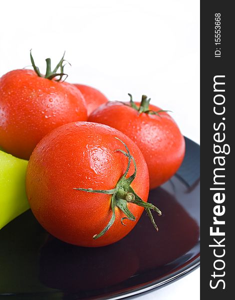Fresh tomatoes washed and placed in a black ceramic plate isolated on white background