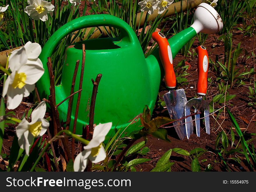 Green Watering Can With Gardening Equipment Behind