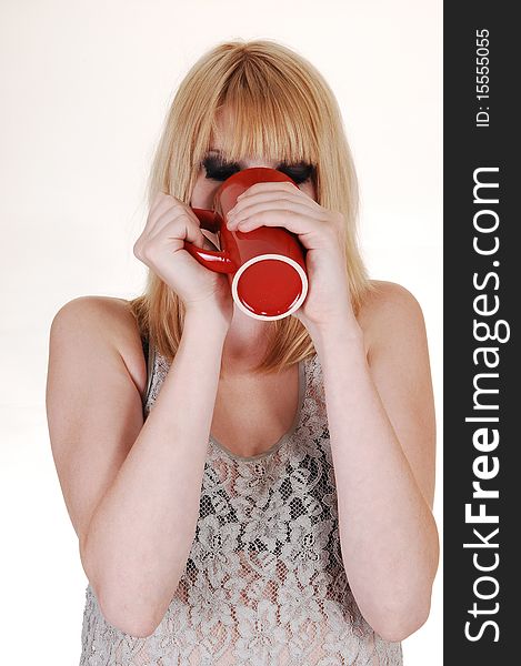 An blond young woman, very thirsty, thinking coffee from an red cup and standing in the studio for white background. An blond young woman, very thirsty, thinking coffee from an red cup and standing in the studio for white background.