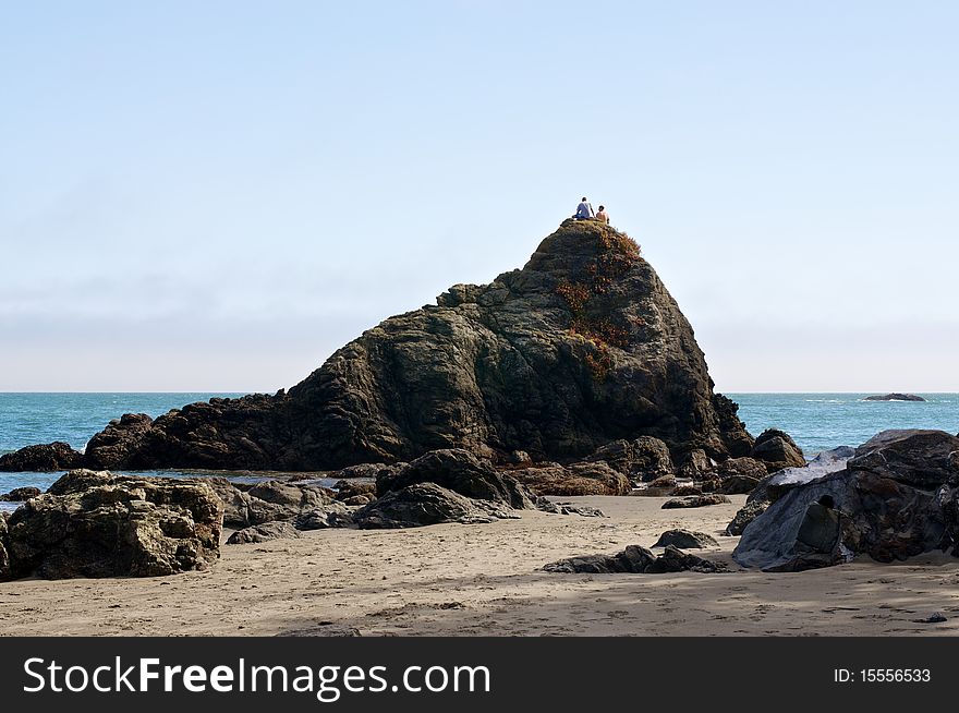 Two people sitting atop a very large rock on a California beach. Two people sitting atop a very large rock on a California beach.