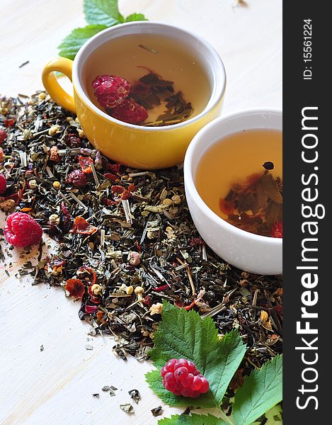 Two cups herbal tea is brewed in which,  alongside dry tea and berries of raspberry