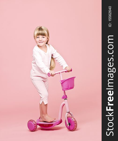 Young girl with a scooter towards pink background