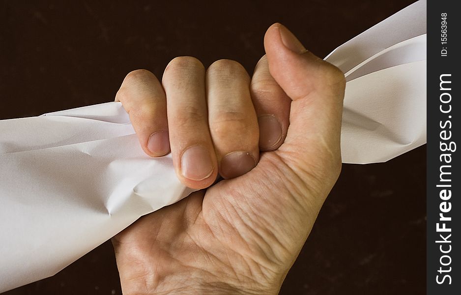 The hand squeezes a piece of paper against a dark background. The hand squeezes a piece of paper against a dark background