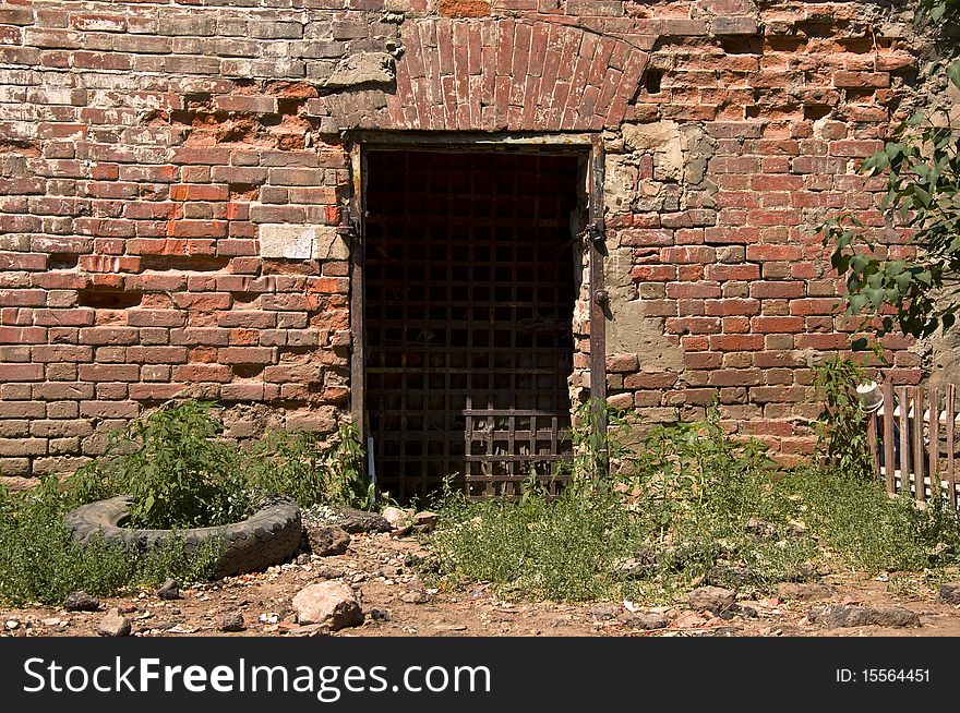 Old door with iron bars in a dilapidated brick wall.