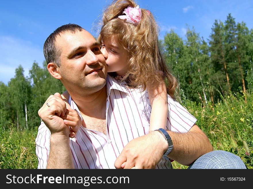 The daughter embraces the daddy and kisses him on a cheek in the summer on the nature. The daughter embraces the daddy and kisses him on a cheek in the summer on the nature