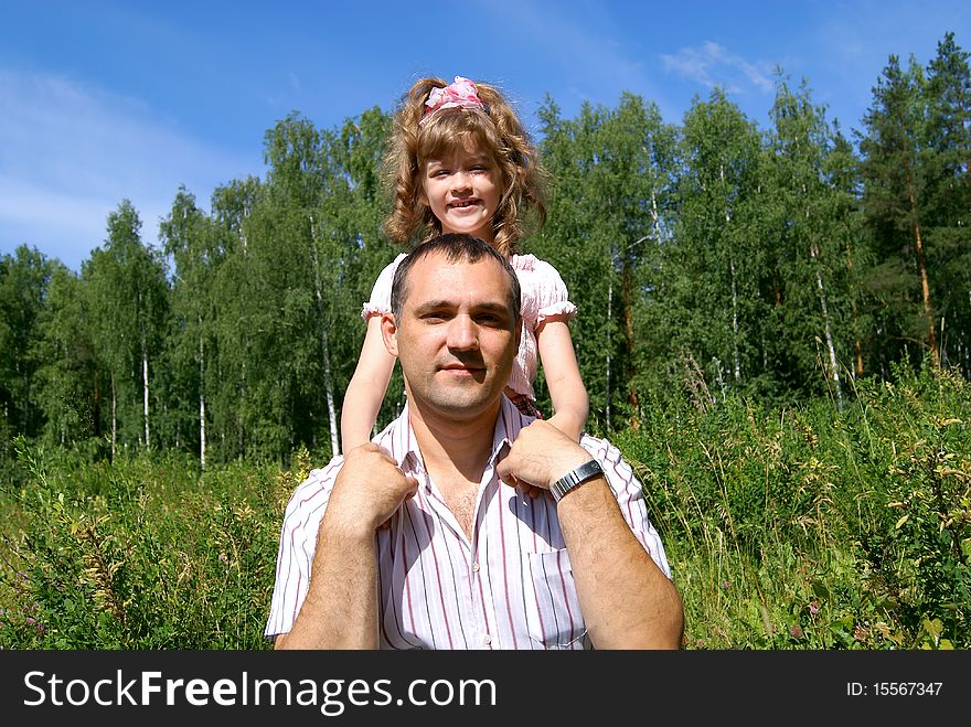 In the summer against the sky, a green grass and trees the smiling daughter embraces the daddy. In the summer against the sky, a green grass and trees the smiling daughter embraces the daddy