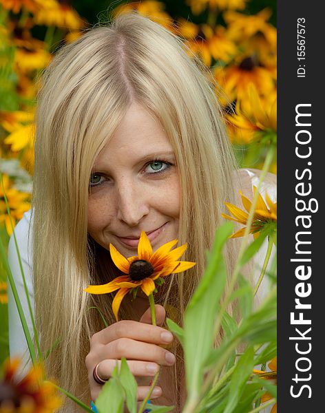 Young blond woman with blue eyes holding a yellow cone-flowers flower and smiling. Young blond woman with blue eyes holding a yellow cone-flowers flower and smiling.