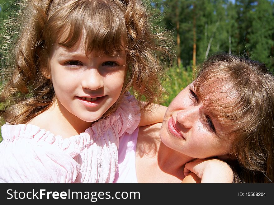In the summer on the nature the beautiful girl embraces  mother who looks at her. In the summer on the nature the beautiful girl embraces  mother who looks at her