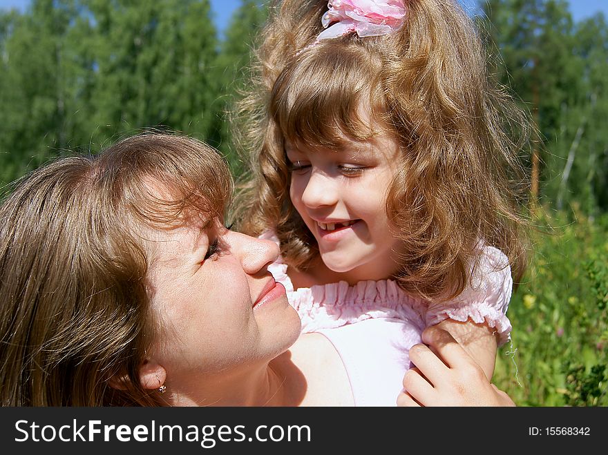 The laughing beautiful girl embraces the woman in the summer on the nature and looks at it. The laughing beautiful girl embraces the woman in the summer on the nature and looks at it