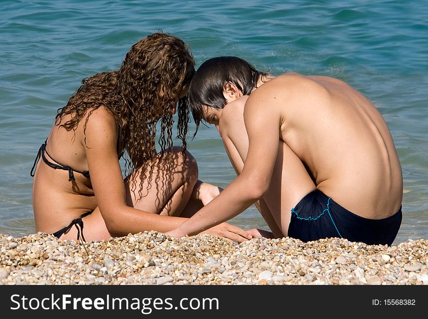 Boy and girl on the beach looking for beautiful pebbles deregu