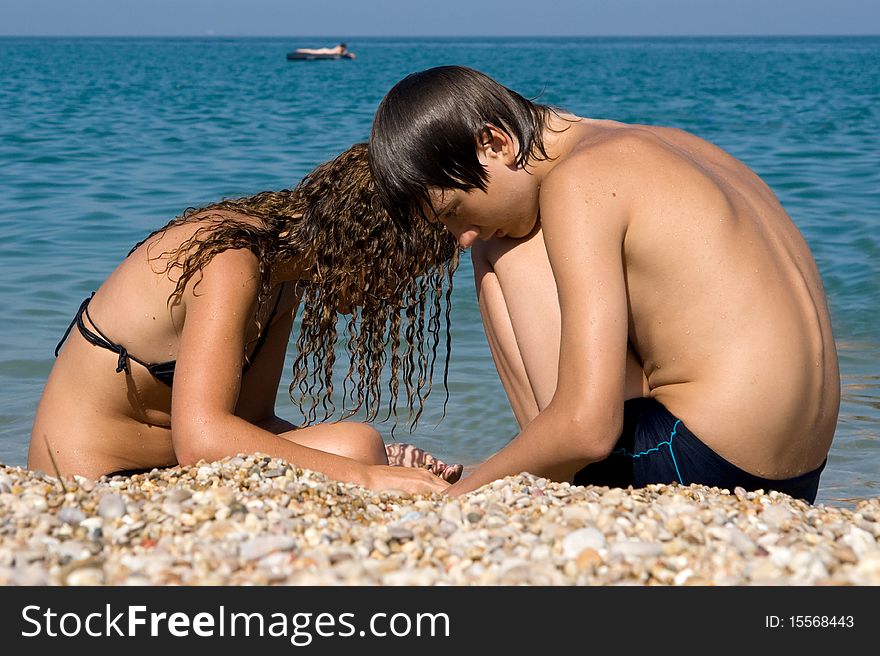 Boy and girl on the beach looking for beautiful pebbles deregu