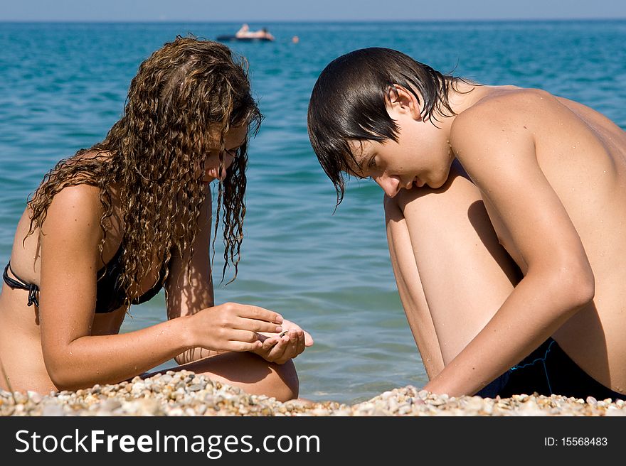 Boy and girl on the beach looking for beautiful pebbles deregu