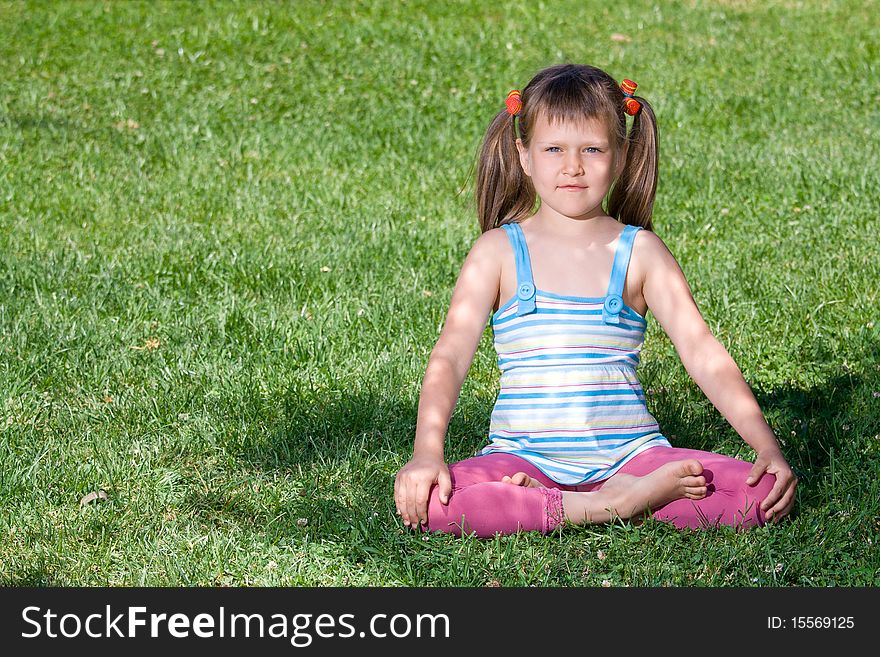 Cute little girl is sitting in yoga lotus asana under tree shadow on the green grass. Cute little girl is sitting in yoga lotus asana under tree shadow on the green grass